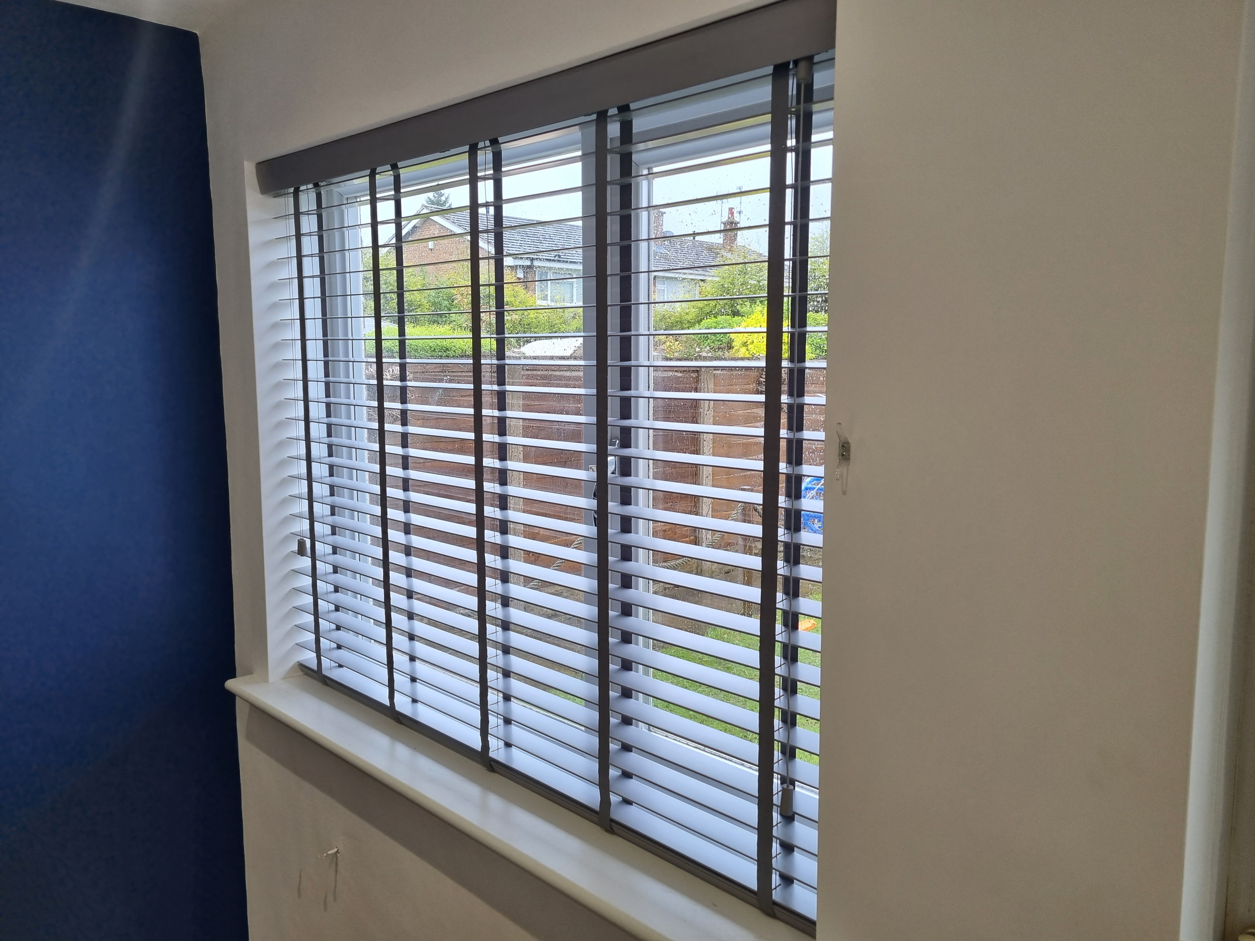 Faux wood venetian blinds with a warm timber-effect finish, garden view
