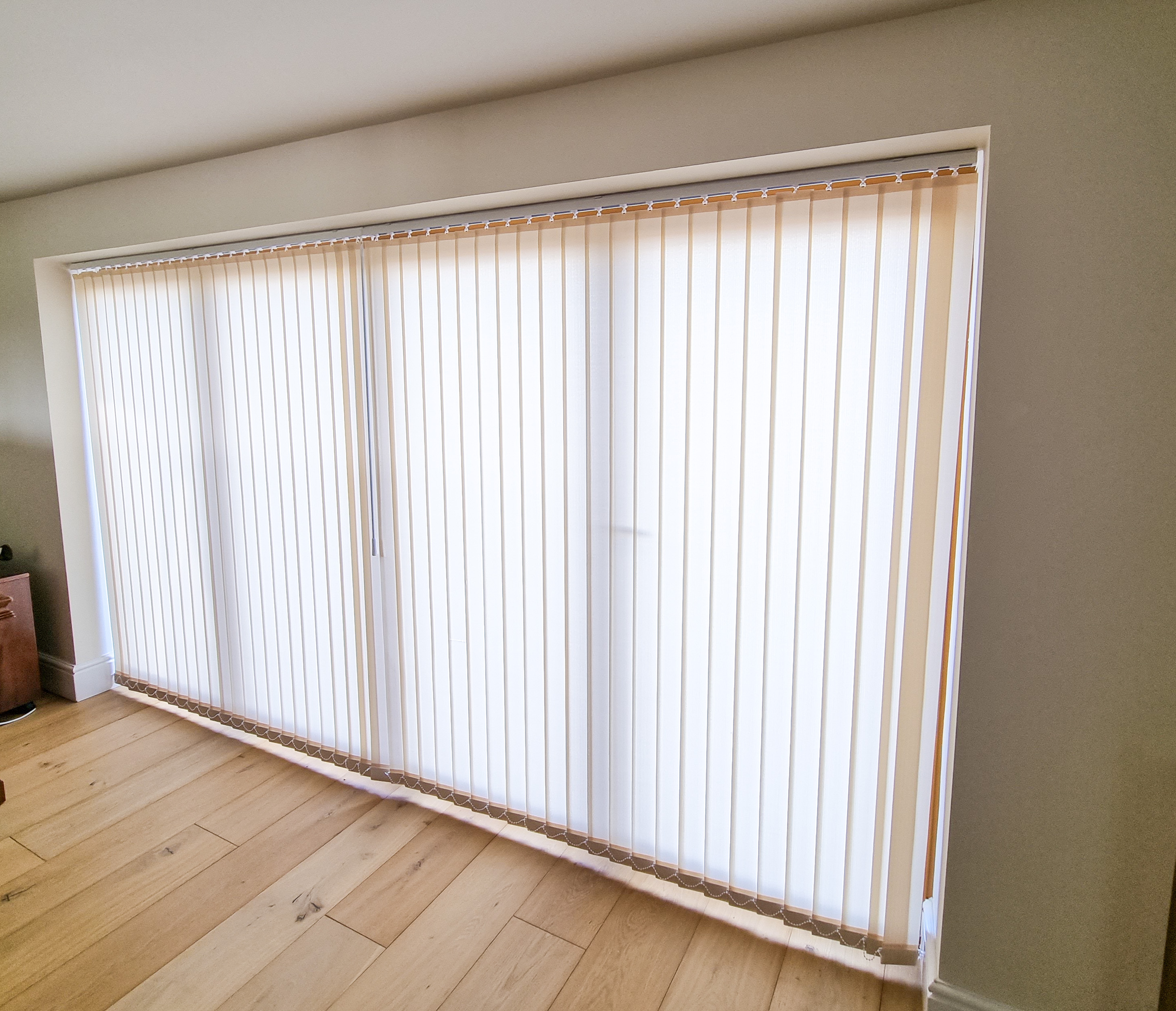 Cream vertical blinds fitted to a wide window in a bright, modern room