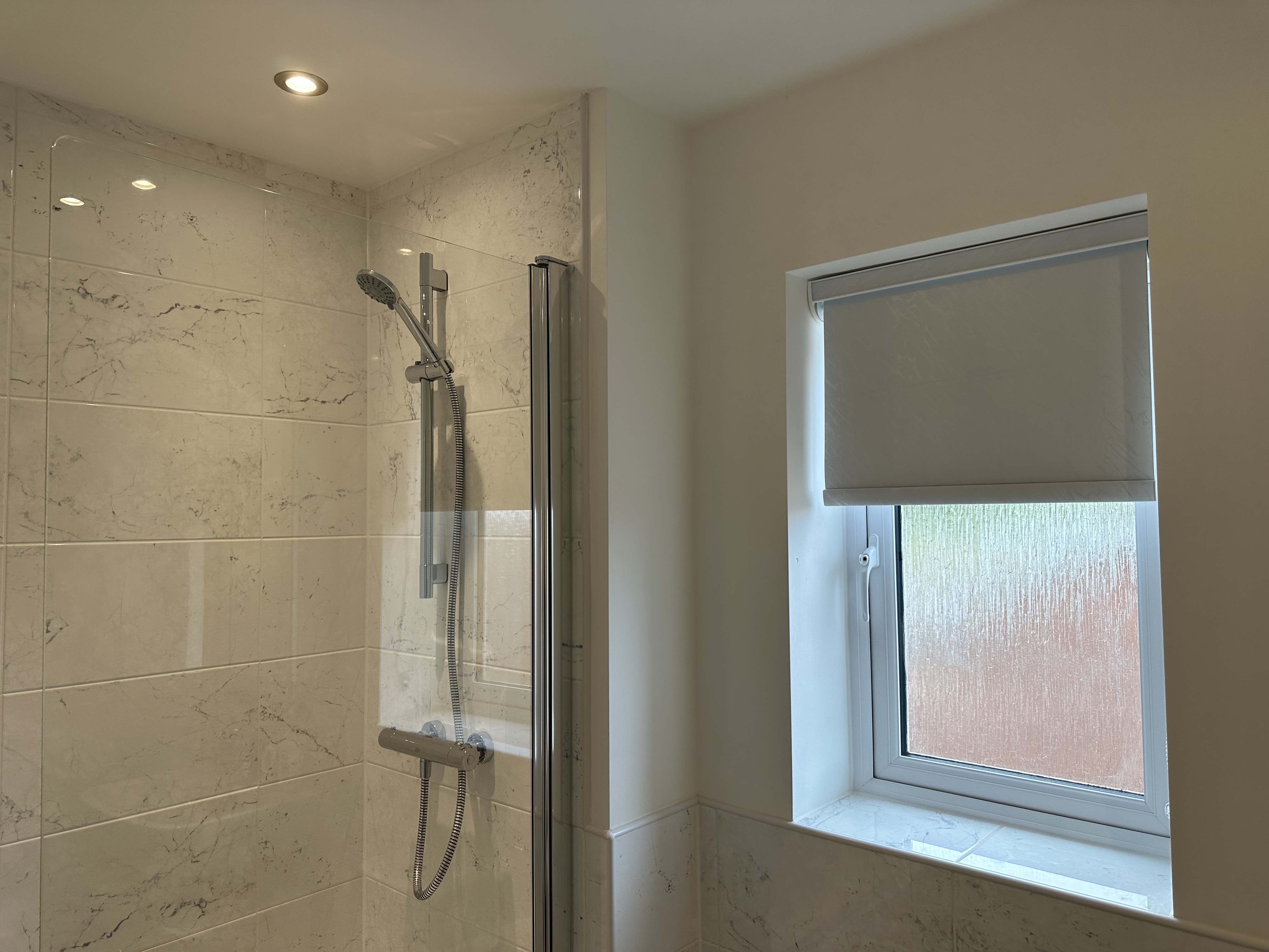 Grey roller blind fitted to a bathroom window with obscured glass